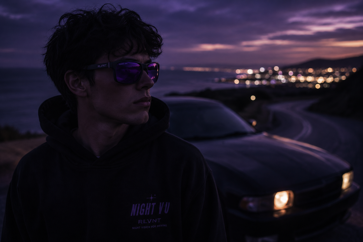 Driver wearing purple-toned RLVNT Night VU glasses near a car at dusk with coastal road lights softly blurred in the background.